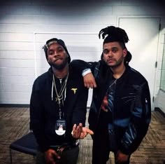 two young men standing next to each other in an empty room, one with dreadlocks on his head