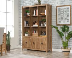 a wooden bookcase with many books and plants on it in front of a brick wall