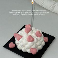 a white cake with pink hearts on it and a candle sticking out of the top