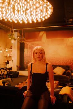 a woman sitting on top of a couch in a room with chandelier above her