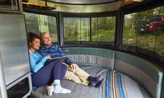 a man and woman are sitting on the bed in a bus looking out the window