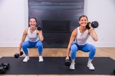 two women are doing squats with dumbbells in front of a fire place