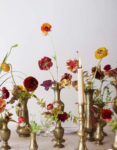 a table topped with lots of vases filled with flowers next to a lit candle