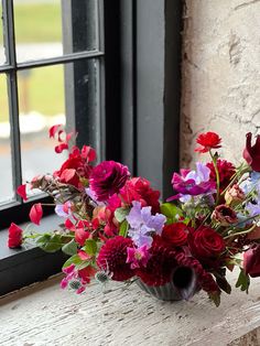 a vase filled with red and purple flowers sitting on top of a window sill