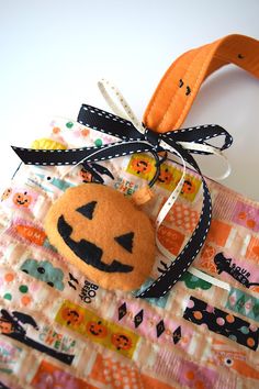 an orange and black pumpkin hanging on a piece of fabric with a ribbon around it