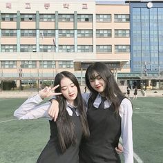 two young women standing next to each other in front of a building and pointing at the camera