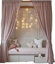 a white bed with pink curtains and lights on the wall above it, in front of a window