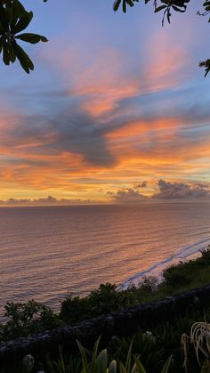 the sun is setting over the ocean with clouds in the sky and trees on the shore