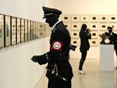 a man dressed in black standing next to a white wall with pictures on the walls