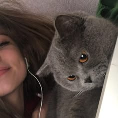 a woman with headphones is next to a gray cat and has ear buds in her ears