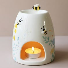 a white ceramic tea light holder with bees on it and a yellow candle in the center