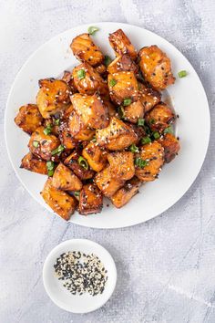 a white plate topped with chicken and sesame seeds next to a bowl of seasoning