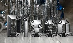 the word disco is surrounded by balloons and streamers in front of a silver curtain