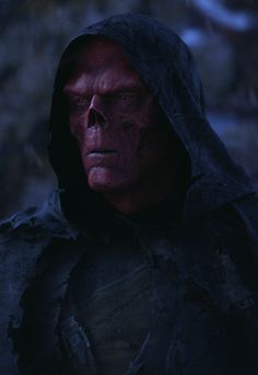 a man with red eyes and a hood on, in the middle of a dark forest