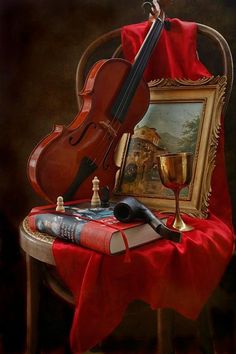 a violin sitting on top of a table next to a wine glass and book with a painting in the background