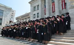 a large group of people in graduation gowns standing on steps near a building with columns