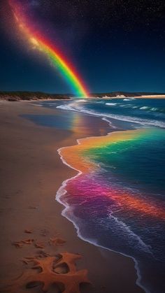 there is a rainbow in the sky over the water and sand on the beach at night