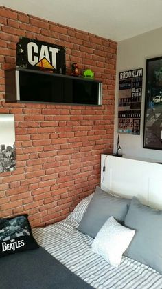 a bedroom with a brick wall and white bedding, black framed pictures on the wall