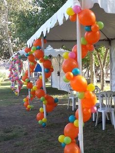 many balloons are hanging from the ceiling in an outdoor event tent with white tables and chairs