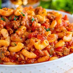 a white bowl filled with pasta and meat covered in sauce on top of a wooden table