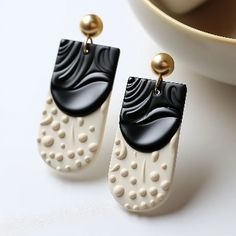 two pairs of black and white earrings sitting on top of a table next to a cup