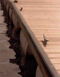 birds are sitting on the edge of a dock in the middle of the water and one bird is perched on the end of the pier