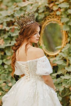 a woman wearing a white dress and a crown standing in front of ivy covered wall