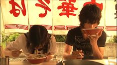 two people sitting at a table eating food with chopsticks in front of them