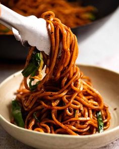 someone is lifting noodles from a bowl with chopsticks