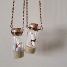 two glass bottles filled with sand and sea shells on a chain hanging from a wall