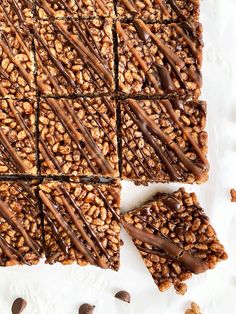 chocolate peanut butter granola bars with drizzled on top and nuts scattered around them