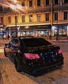 a black car is parked on the side of the road at night in front of a building