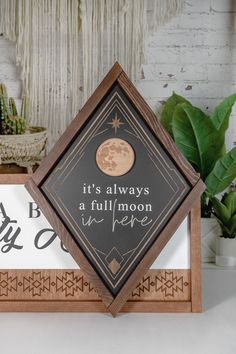 a wooden frame with a quote on it sitting next to a potted plant and wall hanging