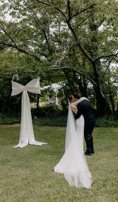 a bride and groom kissing in front of white draping on the grass at their outdoor wedding ceremony