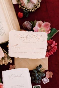 the wedding stationery is laid out on top of an open book and surrounded by flowers