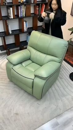 a woman standing next to a green leather chair in a room with bookshelves