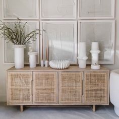 a white vase sitting on top of a wooden cabinet next to pictures and plants in front of it