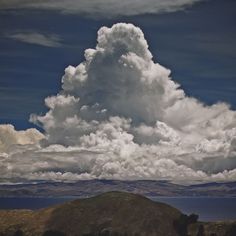 a large cloud is in the sky over some hills and water, with mountains in the background