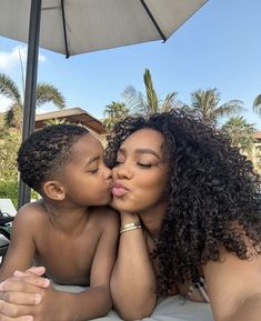 a woman kissing a small child on the cheek with an umbrella over her head and palm trees in the background