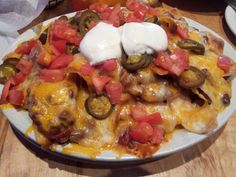 a white plate topped with nachos covered in cheese and toppings on top of a wooden table