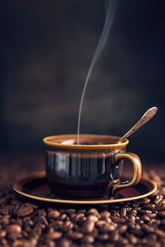 a coffee cup with steam rising out of it sitting on top of some coffee beans