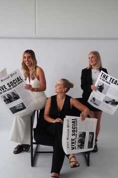 three women sitting on chairs holding newspapers in their hands