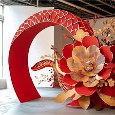 two large red sculptures with flowers on them in an art gallery, one is shaped like a snake and the other is made out of paper