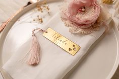 a place setting with a name plate and pink flowers on the table cloth, along with personalized napkins