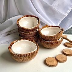 four coconut shell bowls with wooden spoons next to them on a white tablecloth