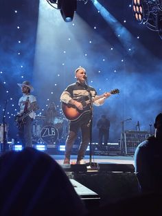 a man standing on top of a stage holding a guitar