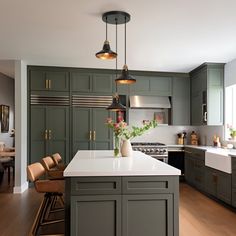 a large kitchen with green cabinets and white counter tops, along with an island in the middle