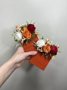 two orange and white flowers are placed on top of an orange piece of paper that is held in someone's hand