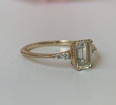 an engagement ring with a green stone and three diamonds on the side, sitting on a white surface