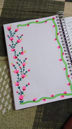 an open notebook with pink flowers and green lines on the cover is sitting on a table